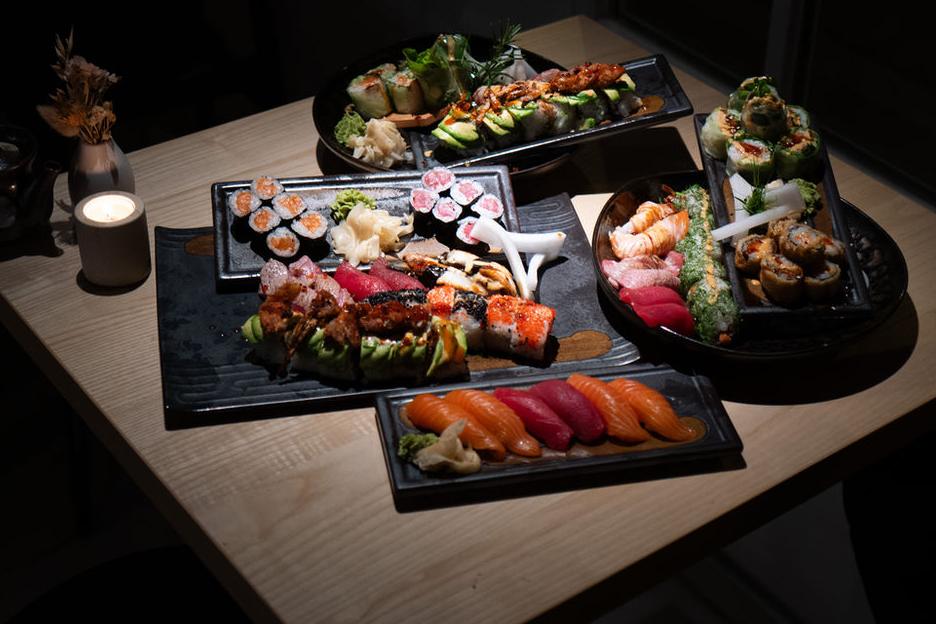 Mehrere Sushi-Platten mit Nigiri, Rollen und Maki auf einem Holztisch